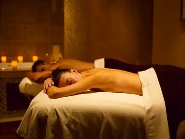 Two guests resting face down on side-by-side tables in a warm, candle-lit room